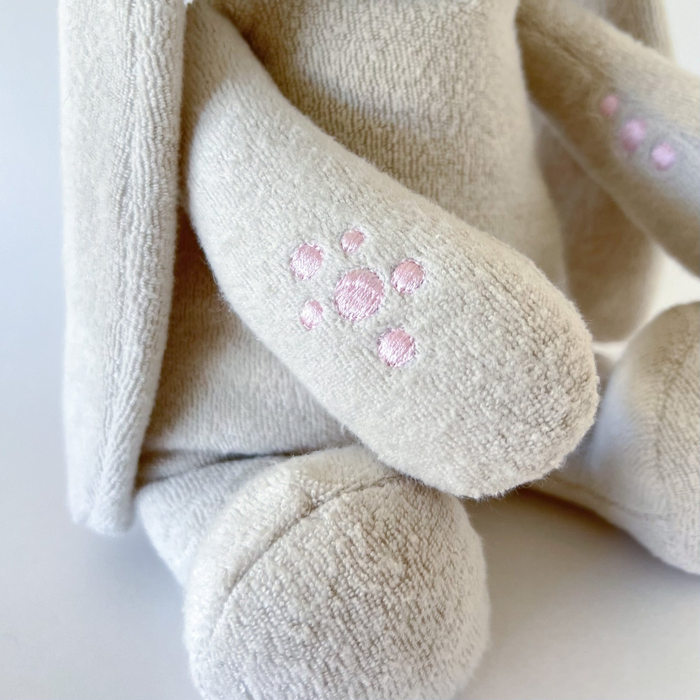 close up shote of stuffed animal showing fuzzy off white arms and embroidered pink circlular patches on arm