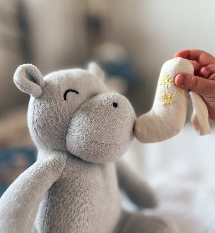 Organic cotton stuffed animal hippo with a child's hand holding a plush inhaler to hippo's mouth practicing asthma treatment