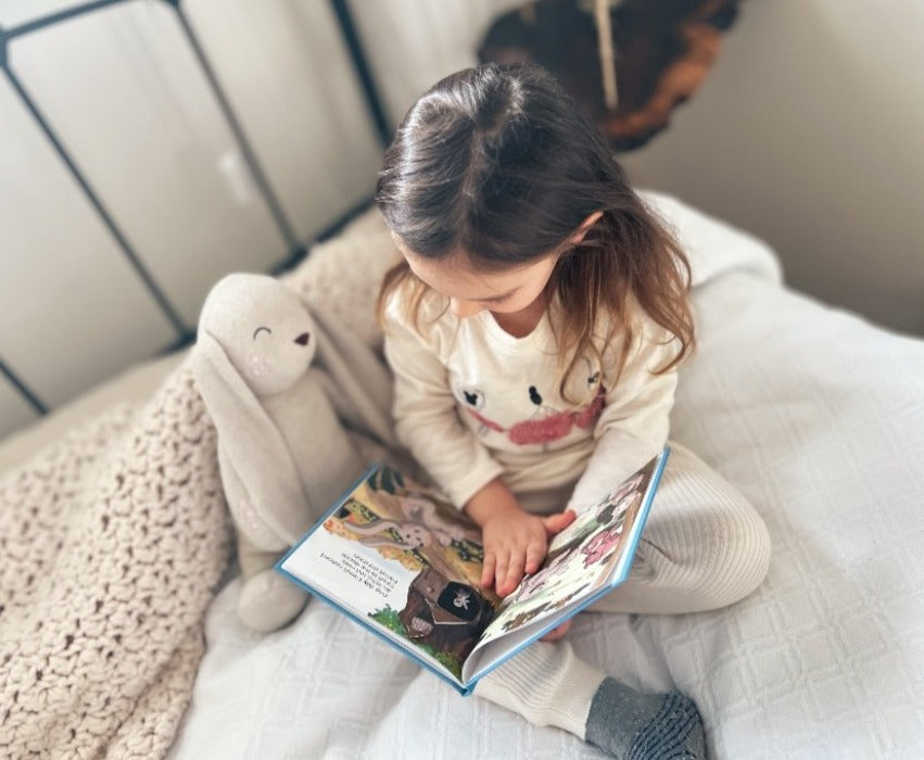 Child sitting beside a stuffed animal bunny on a bed reading book titled Biscuit's Eczema Journey