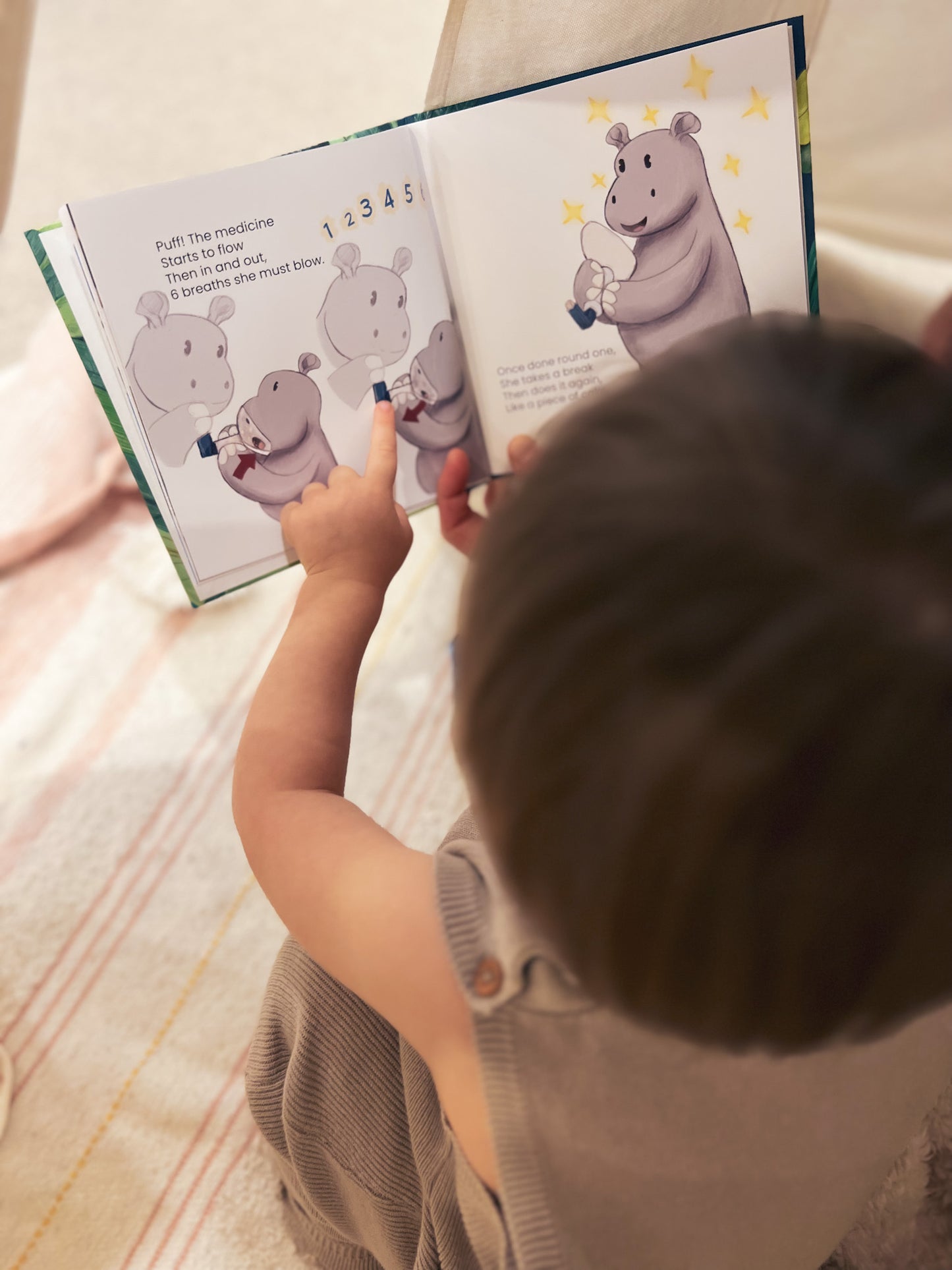 child reading a book and pointing to an illustration of a hippo using in inhaler