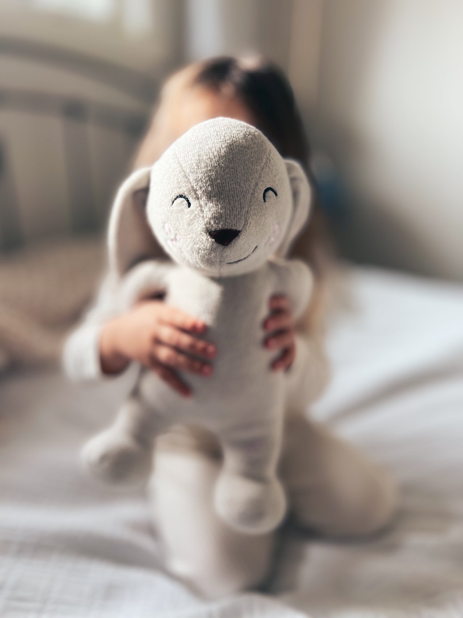 girl blurred in background holding a bunny stuffed animal up to the camera 