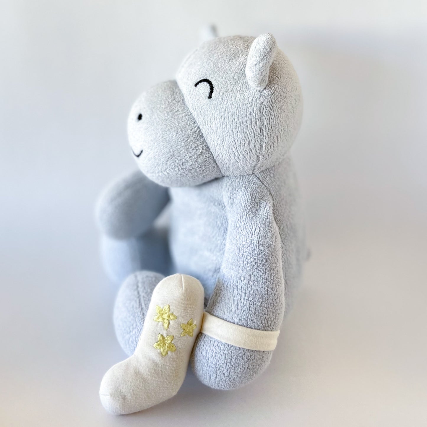 side view of a hippo plush toy with an inhaler strapped to arm
