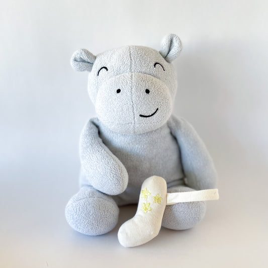 blue hippo stuffed animal sitting with a plush toy inhaler propped on foot