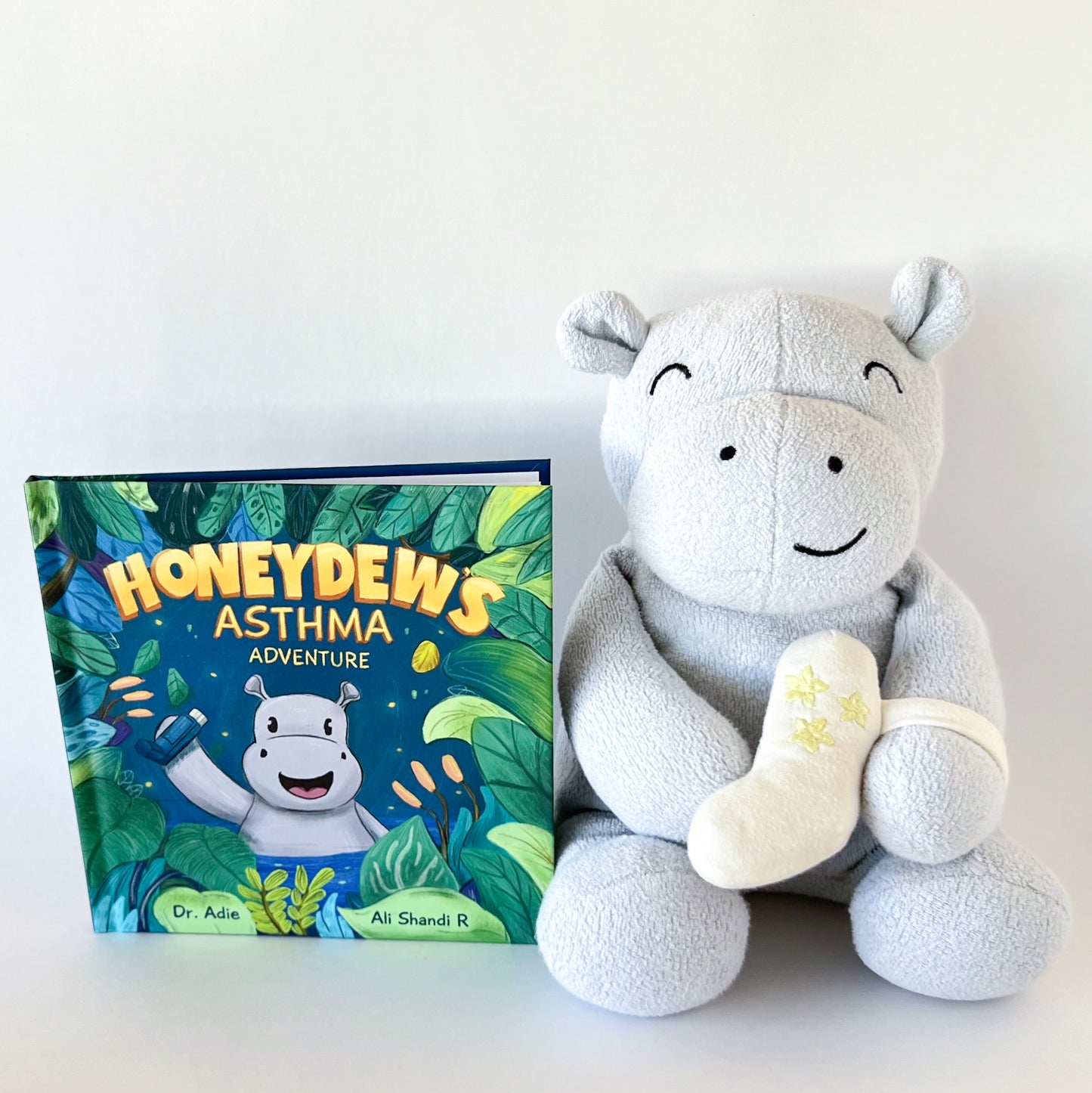 hippo stuffed animal with plush inhaler strapped to arm sitting beside a book with a hippo on the cover titled: honeydew's asthma adventure
